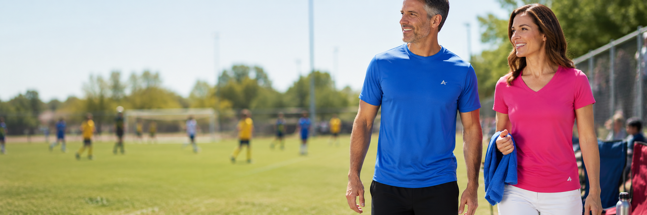 Parents wearing Arctic Cool cooling shirts while watching an outdoor sports game on a hot day