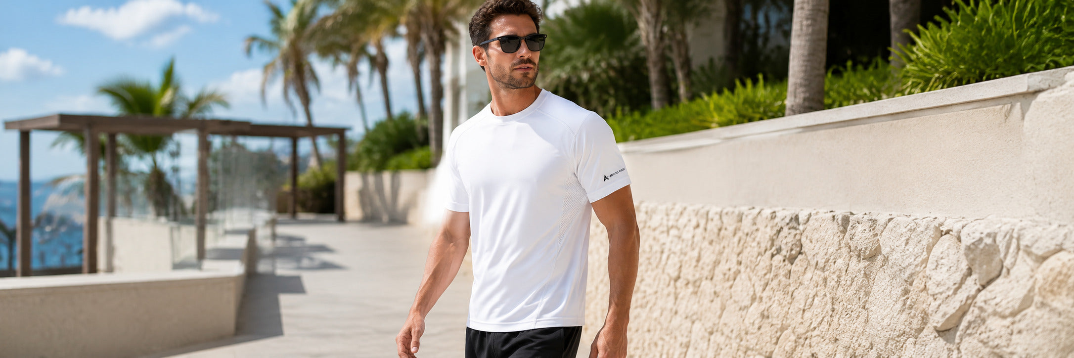 Man wearing a white Arctic Cool Vortex Vent shirt while walking outside in bright summer weather.